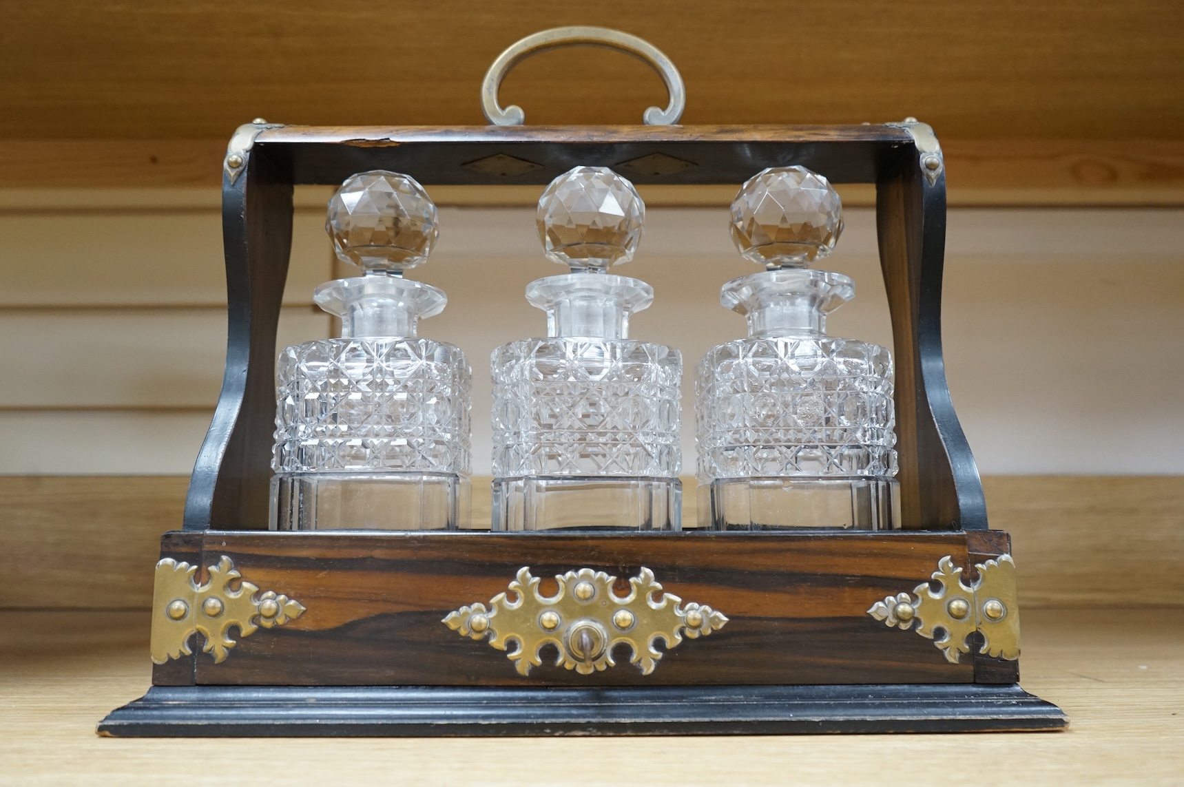 A Victorian coromandel three-bottle tantalus with brass mounts and original key